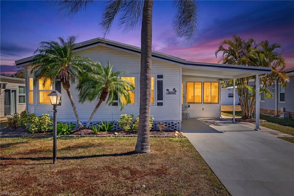 The property features a white exterior with dark shutters, a covered carport, and a well-maintained lawn