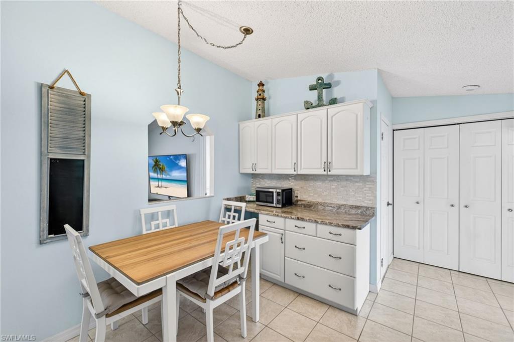 Kitchen with tasteful backsplash, white cabinetry, hanging lights, stainless steel microwave, and light tile patterned flooring