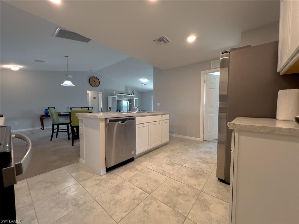 Kitchen with light countertops, white cabinetry, stainless steel appliances, hanging light fixtures, and vaulted ceiling