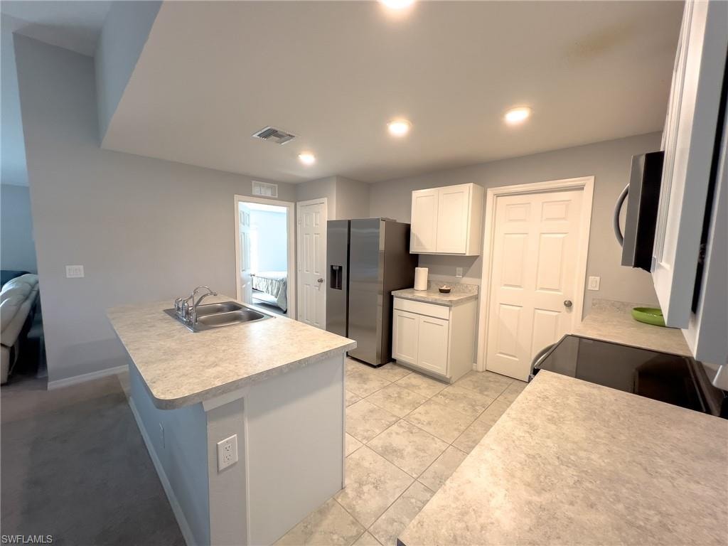 Kitchen featuring white cabinets, light countertops, stainless steel appliances, an island with sink, and recessed lighting