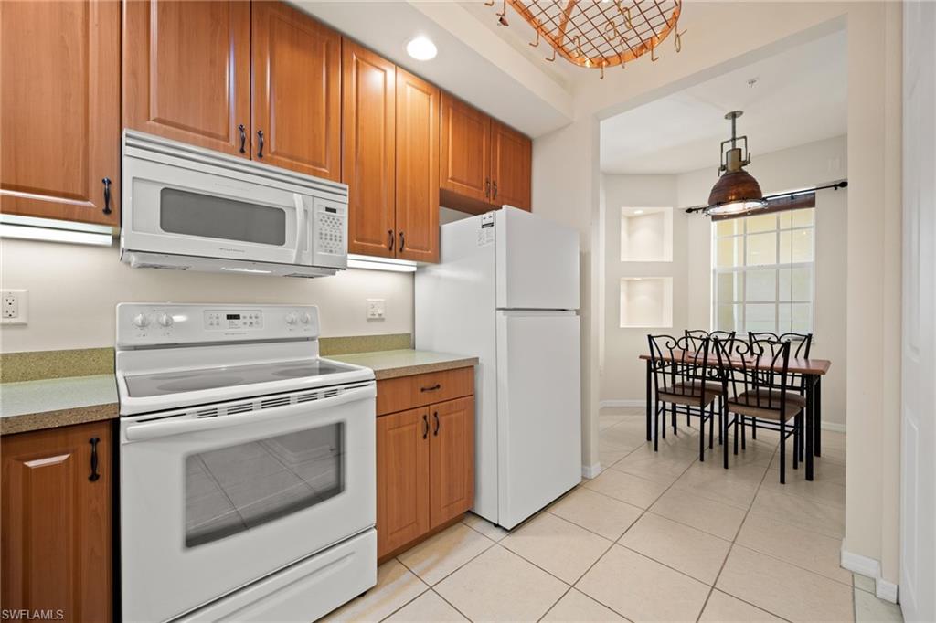 Kitchen to breakfast room with white appliances, wood finish cabinetry, light countertops, and pendant lighting