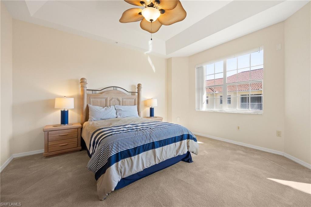 Carpeted bedroom with a tray ceiling and ceiling fan