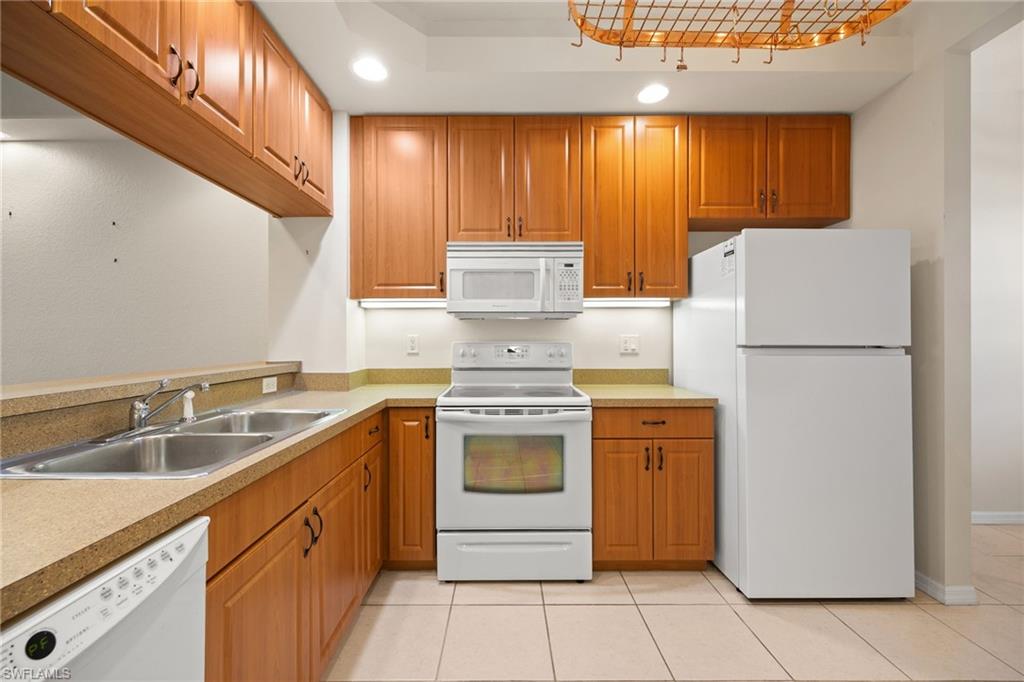 Kitchen from hallway entrance with white appliances, recessed lighting, wood finish cabinets, light countertops, and light tile patterned flooring
