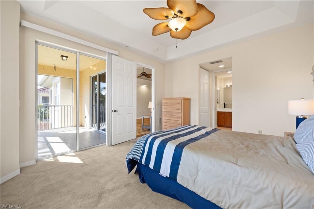 Bedroom featuring carpet, access to exterior, a ceiling fan, a tray ceiling, and ensuite bathroom