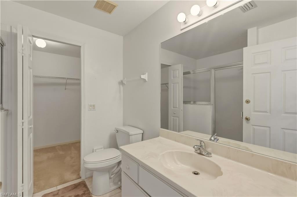 Bathroom featuring vanity, a shower stall, a walk in closet, light colored carpet, and light tile patterned floors