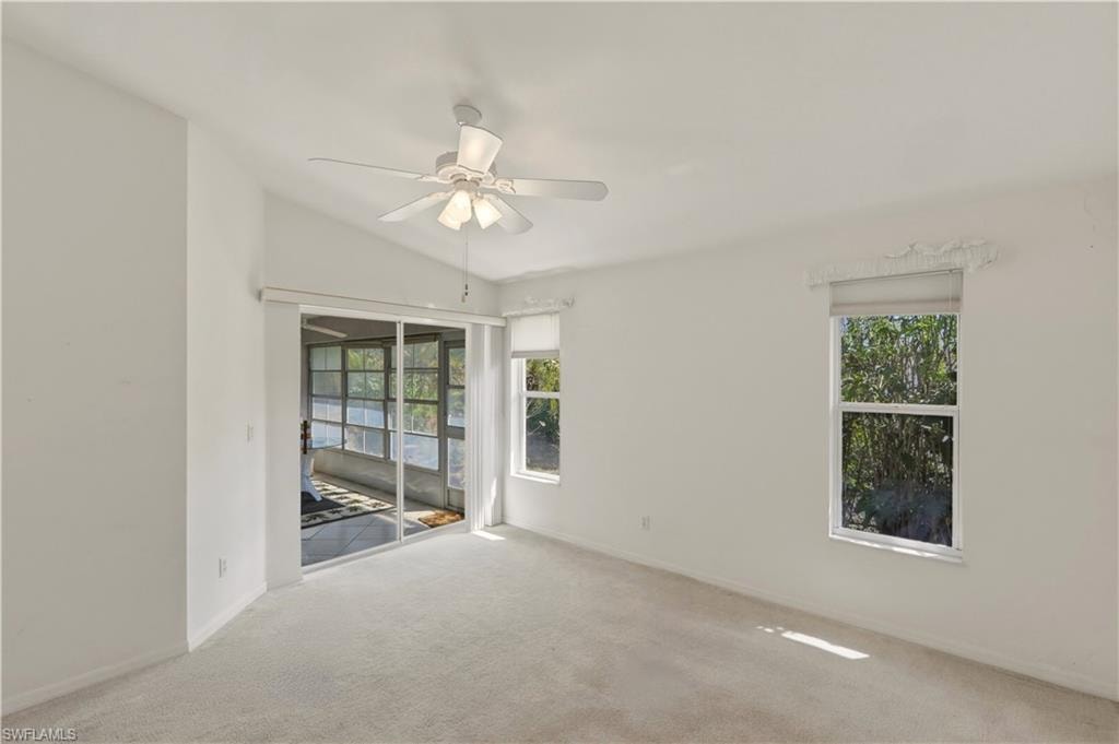 Unfurnished room featuring a ceiling fan, carpet, lofted ceiling, and healthy amount of natural light