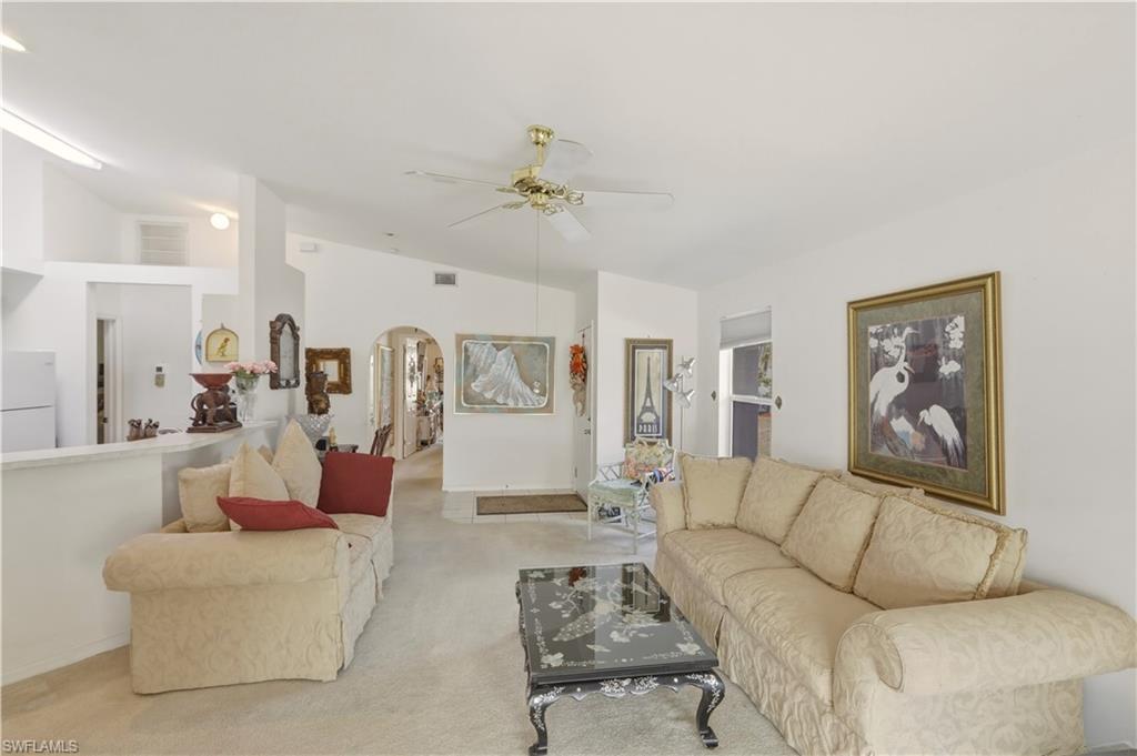 Living area with arched walkways, a ceiling fan, carpet flooring, and lofted ceiling