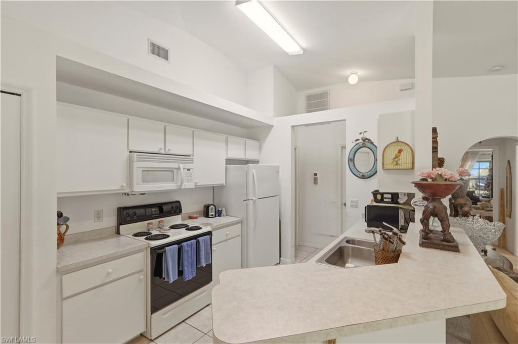 Kitchen featuring white appliances, light countertops, vaulted ceiling, white cabinets, and a kitchen breakfast bar