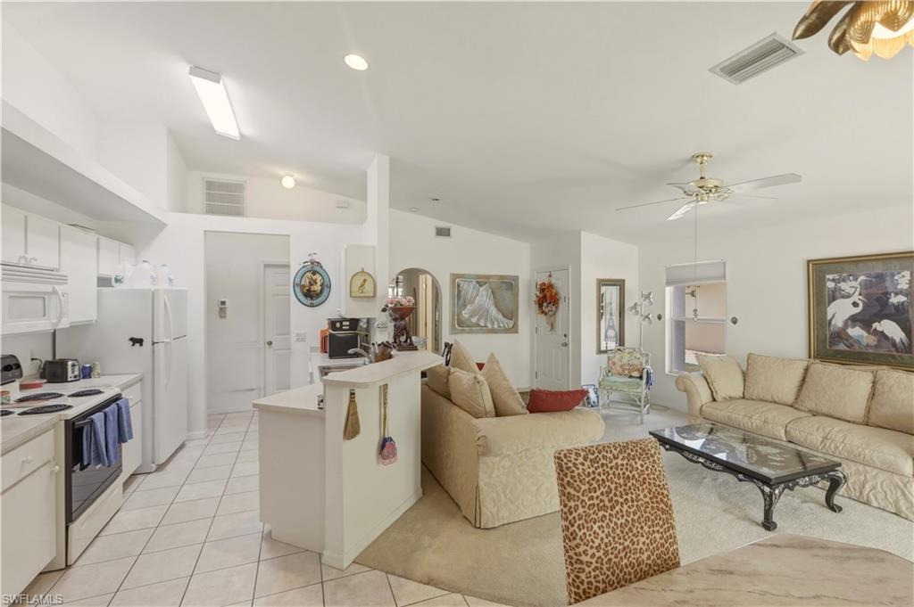 Living room featuring lofted ceiling, a ceiling fan, light tile patterned floors, and arched walkways