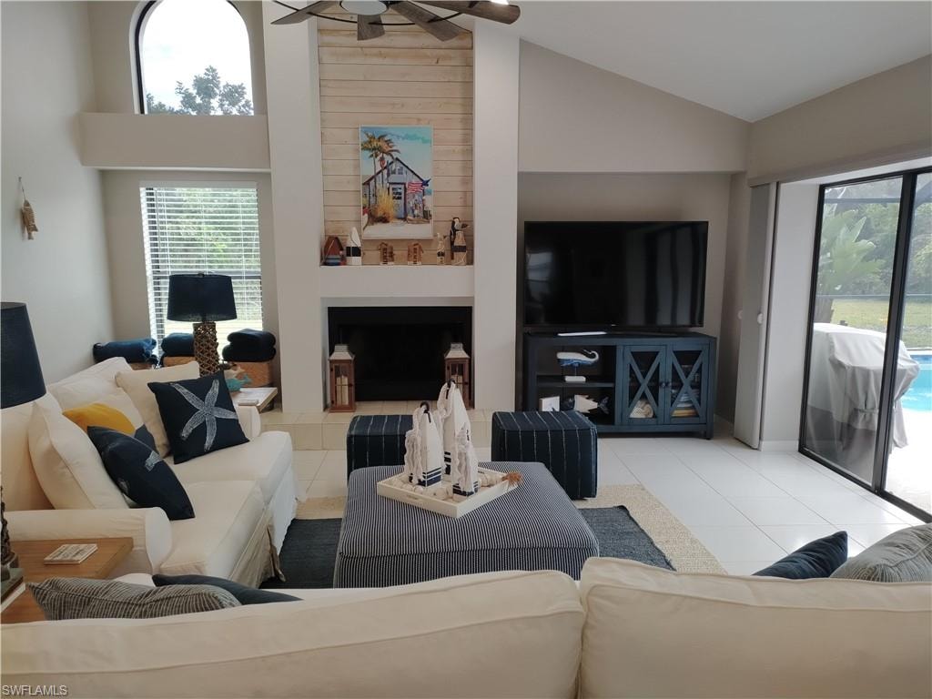 Living area featuring vaulted ceiling, tile patterned floors, a ceiling fan, and a large fireplace