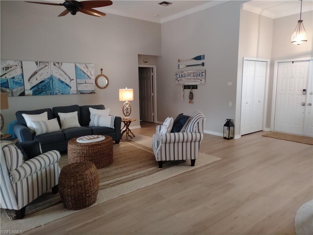 Living area with wood finished floors, a high ceiling, ceiling fan, and ornamental molding