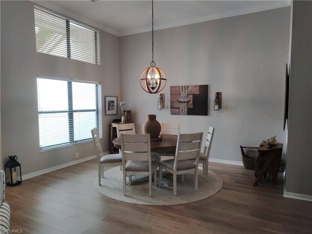 Dining room featuring wood finished floors, hanging lights, crown molding, and a high ceiling