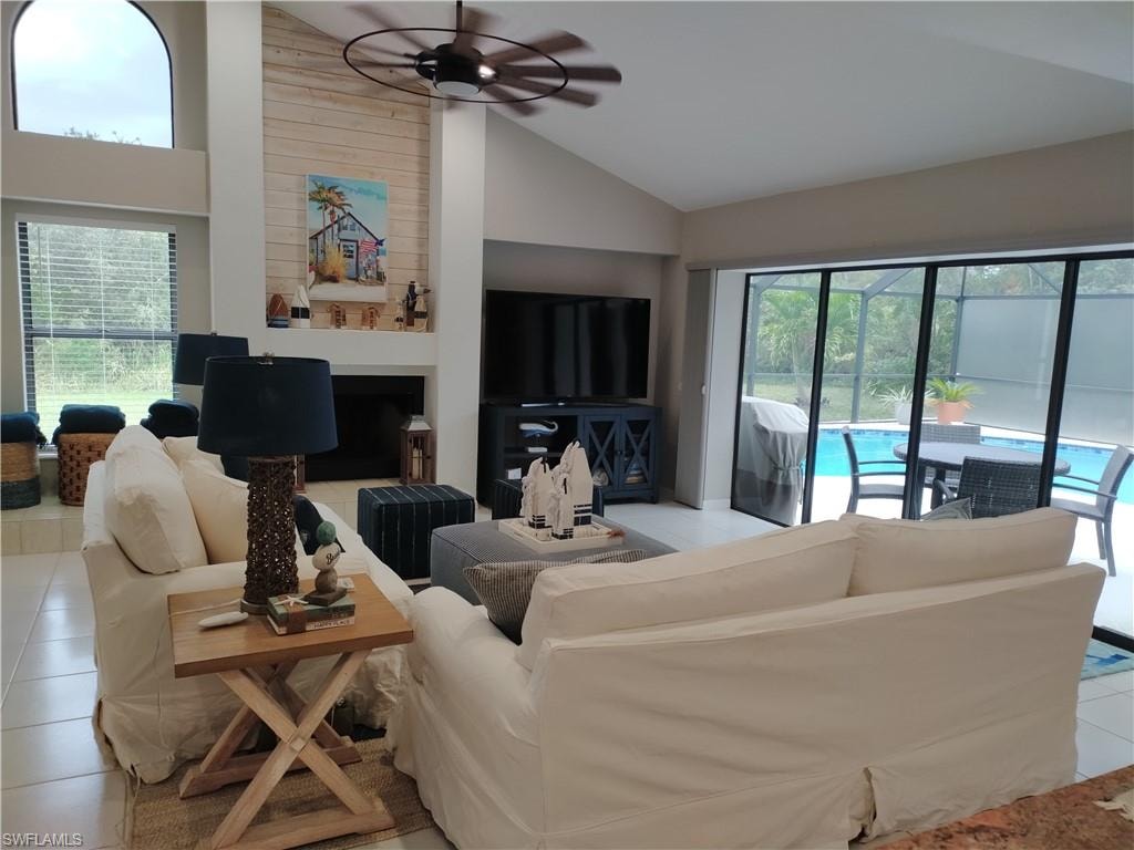 Living room with tile patterned flooring, a ceiling fan, plenty of natural light, vaulted ceiling, and a fireplace