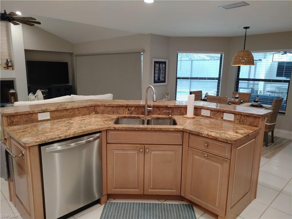 Kitchen featuring dishwasher, light tile patterned floors, light stone countertops, hanging light fixtures, and a center island with sink