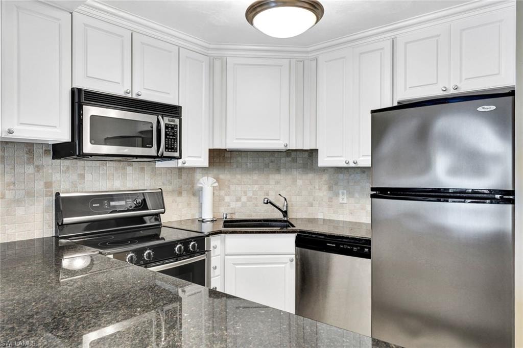 Kitchen with stainless steel appliances, dark stone counters, white cabinets, and decorative backsplash
