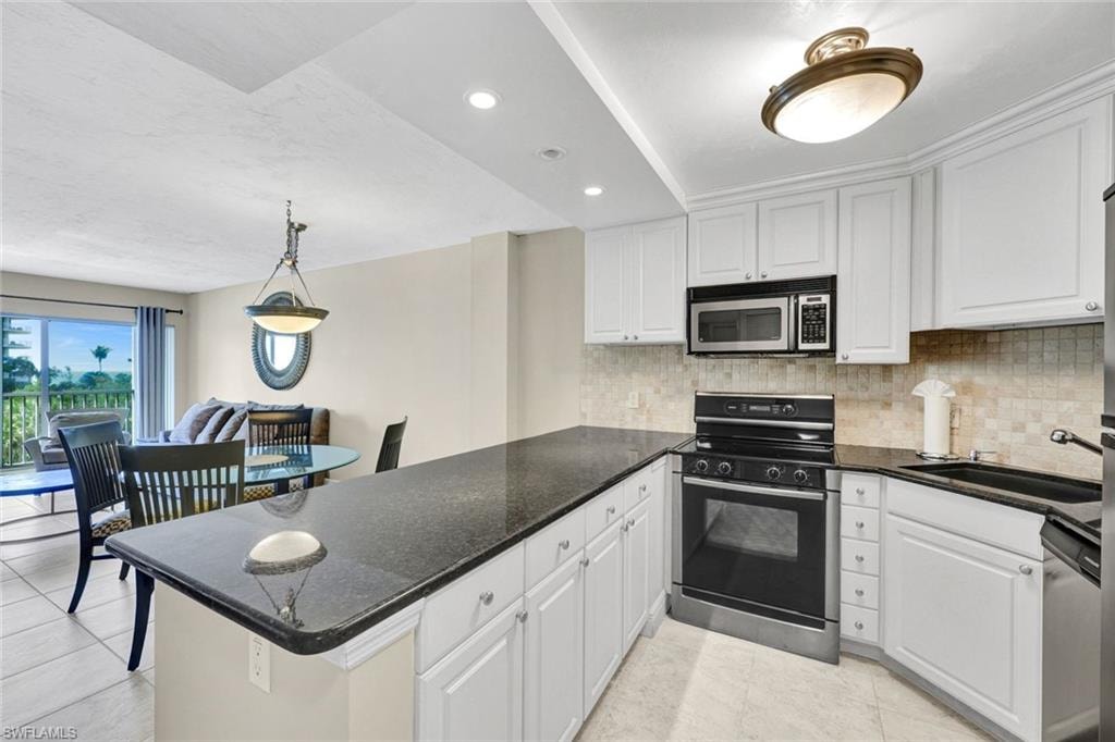 Kitchen with stainless steel appliances, dark stone countertops, decorative light fixtures, backsplash, and white cabinetry