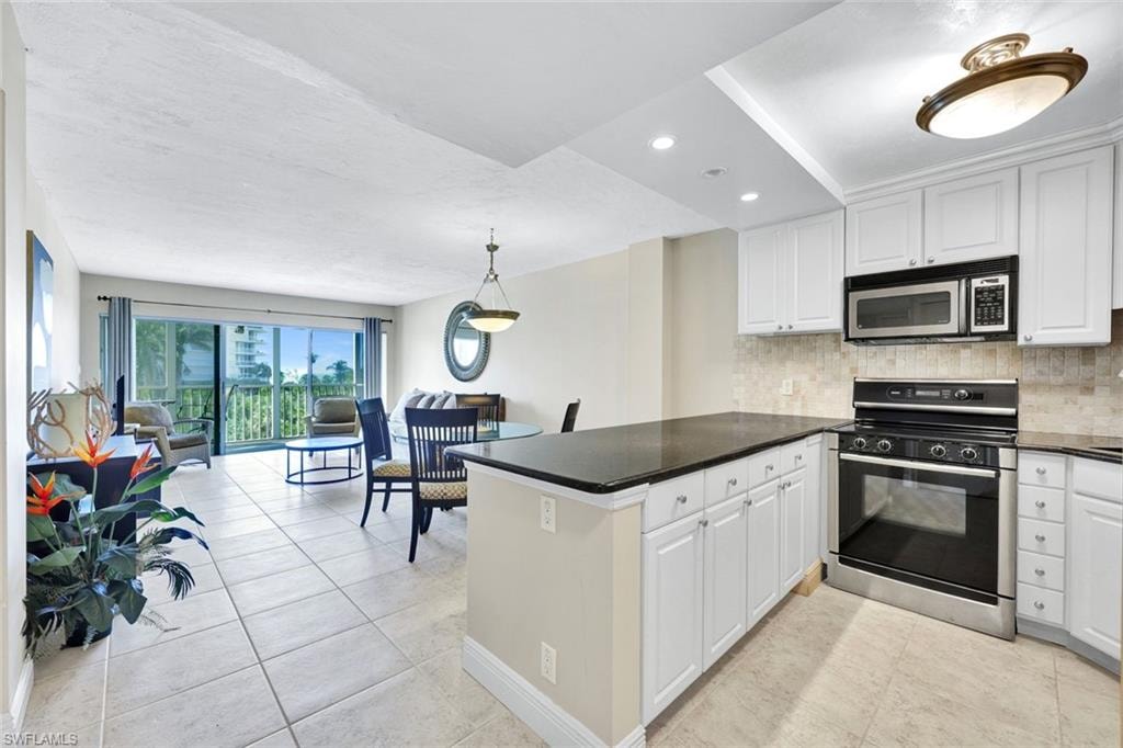 Kitchen with electric range oven, stainless steel microwave, backsplash, and white cabinetry