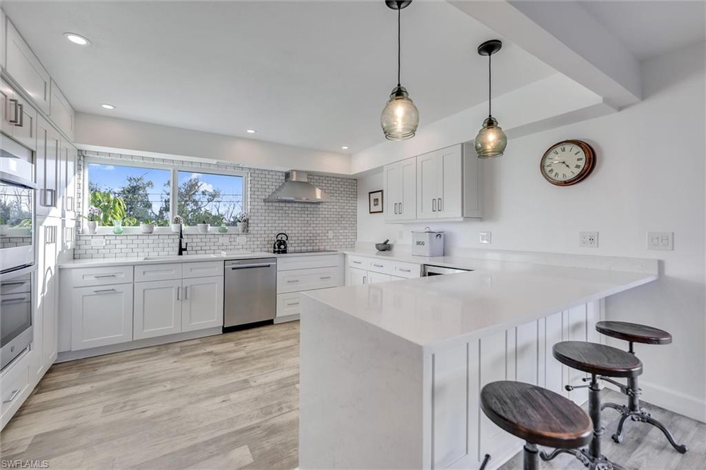 Kitchen with a kitchen breakfast bar, a peninsula, light wood-style flooring, stainless steel appliances, and pendant lighting