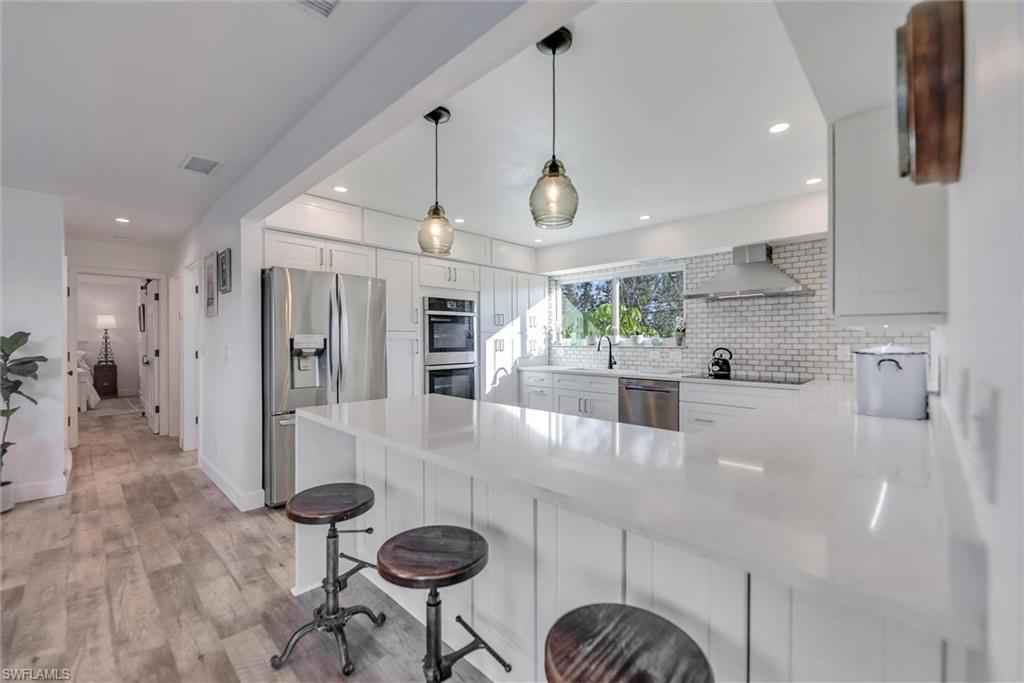 Kitchen with a peninsula, backsplash, stainless steel appliances, a kitchen bar, and white cabinetry