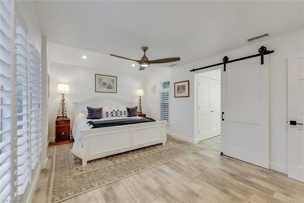 Bedroom with a barn door, light wood-style floors, ceiling fan, recessed lighting, and lofted ceiling
