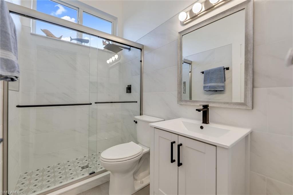 Bathroom featuring a stall shower, vanity, and tile walls