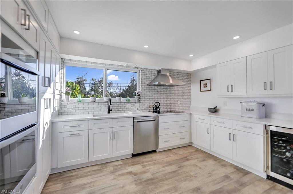 Kitchen with wine cooler, stainless steel appliances, white cabinetry, light wood-style floors, and recessed lighting