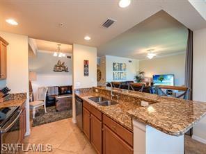 Kitchen with light tile patterned flooring, sink, light stone counters, a center island with sink, and stainless steel appliances