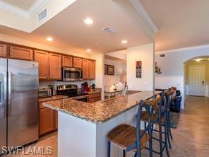Kitchen featuring ornamental molding, stainless steel appliances, a kitchen bar, and dark stone countertops