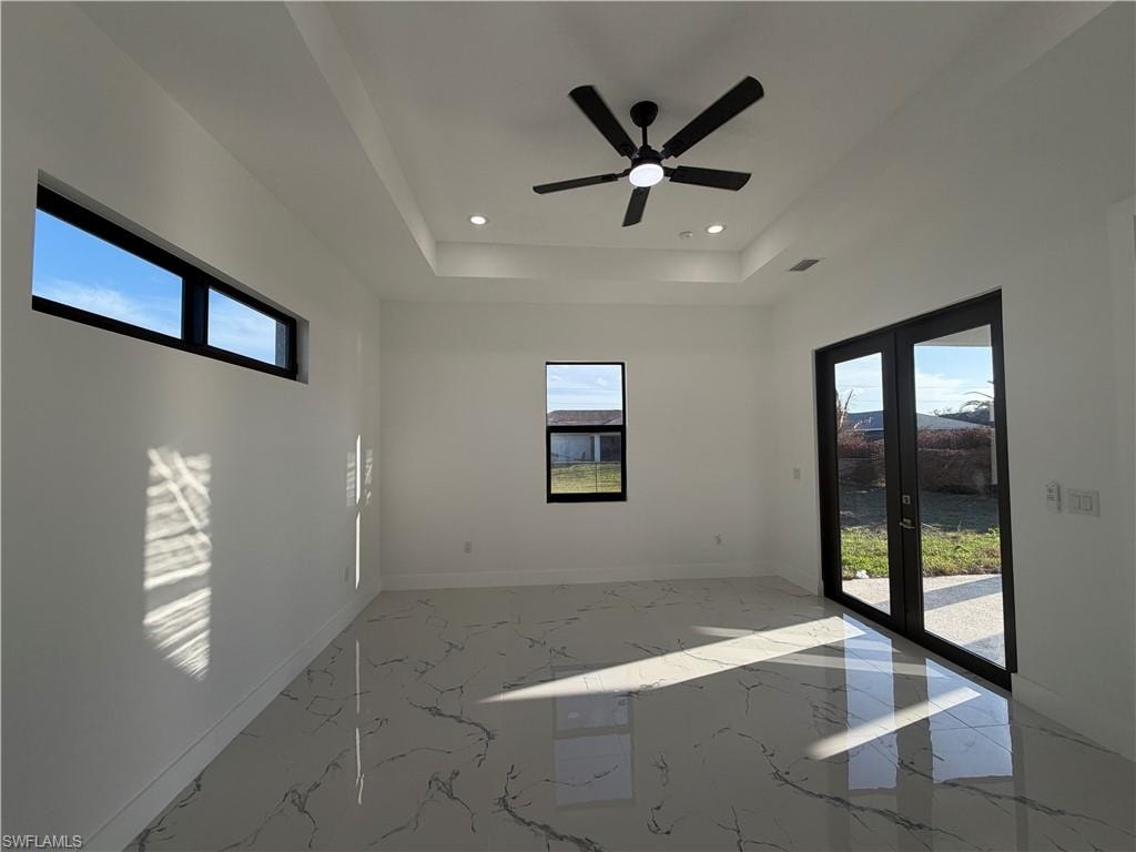 Spare room with light marble finish flooring, plenty of natural light, ceiling fan, recessed lighting, and a tray ceiling