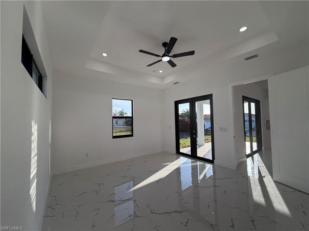 Empty room featuring french doors, recessed lighting, a ceiling fan, light marble finish floors, and a raised ceiling