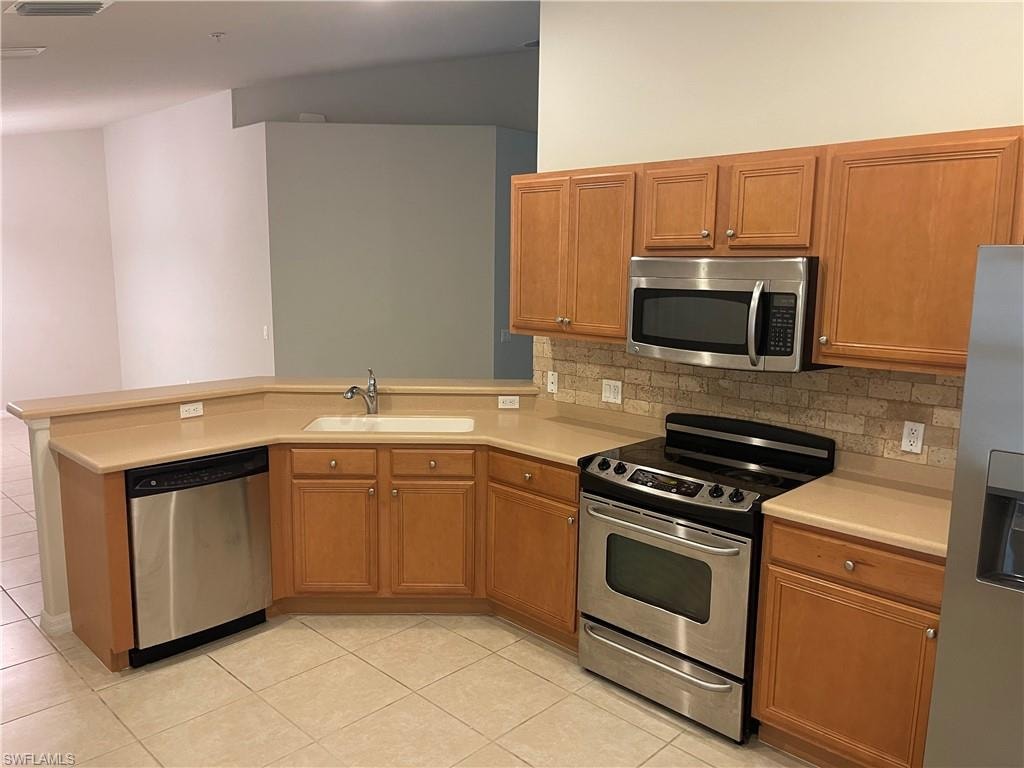 Kitchen featuring stainless steel appliances, a peninsula, light countertops, and wood finish cabinetry