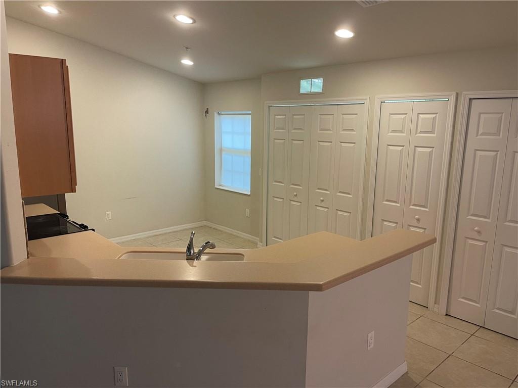 Kitchen featuring a peninsula, light countertops, light tile patterned floors, recessed lighting, and black range with electric cooktop