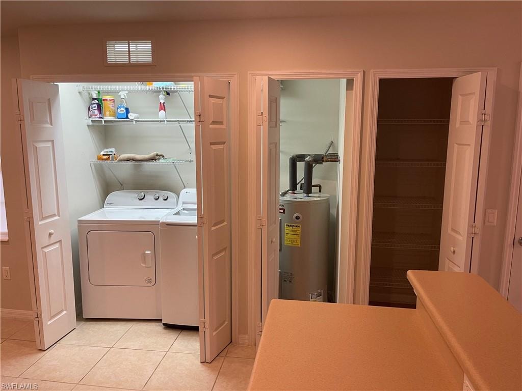 Laundry area featuring water heater, independent washer and dryer, and light tile patterned flooring