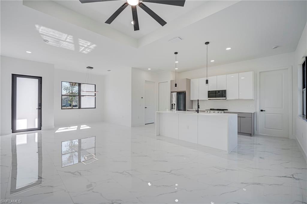 Kitchen featuring decorative light fixtures, white cabinets, open floor plan, light marble finish floors, and a raised ceiling
