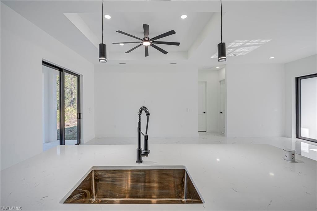 Kitchen with light stone counters, a tray ceiling, hanging light fixtures, and ceiling fan