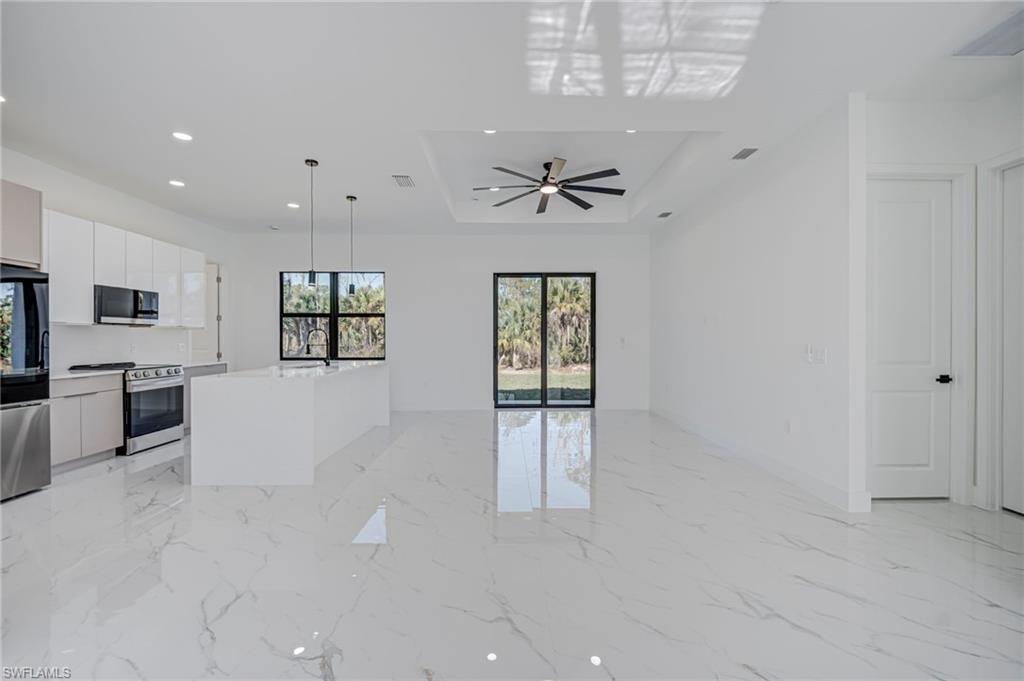 Kitchen with white cabinetry, stainless steel appliances, a kitchen island with sink, modern cabinets, and light marble finish floors