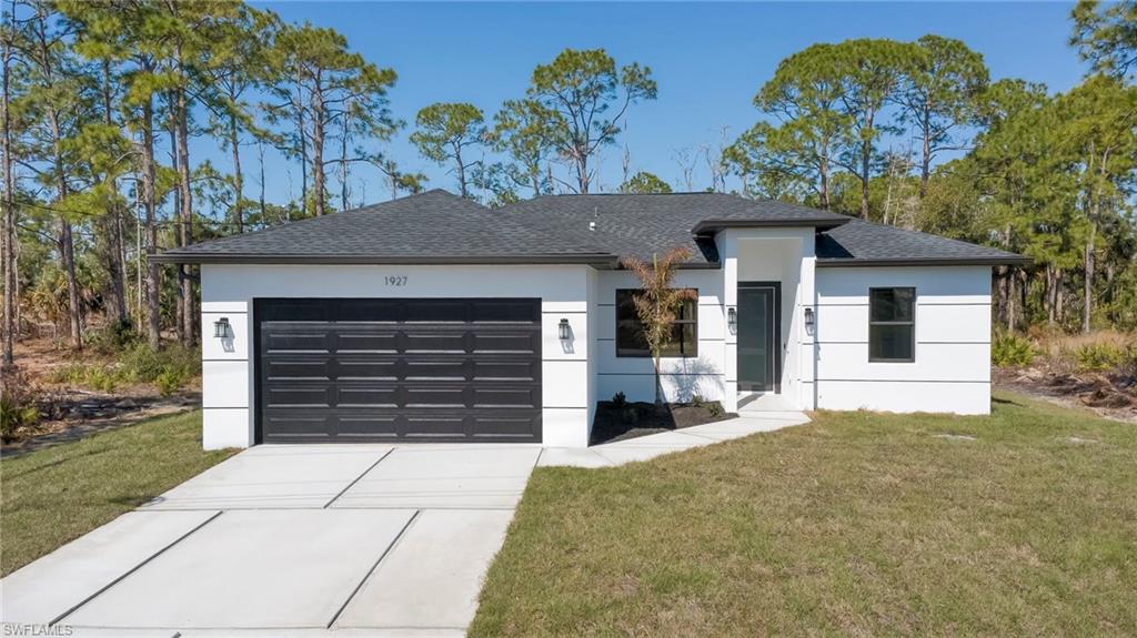 View of front of house featuring a front yard, roof with shingles, a garage, driveway, and stucco siding