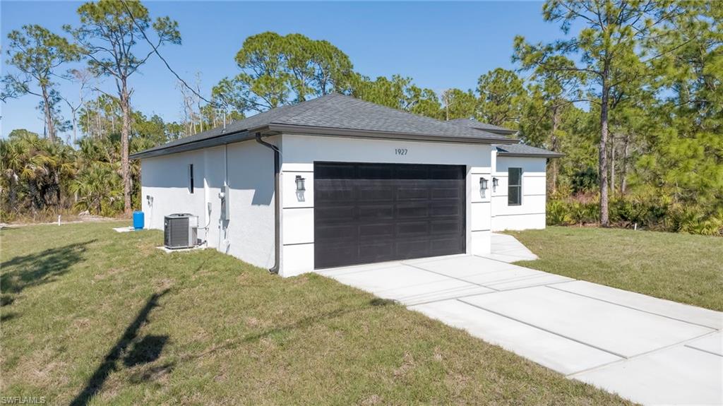 View of side of home with a garage, a lawn, stucco siding, driveway, and a shingled roof