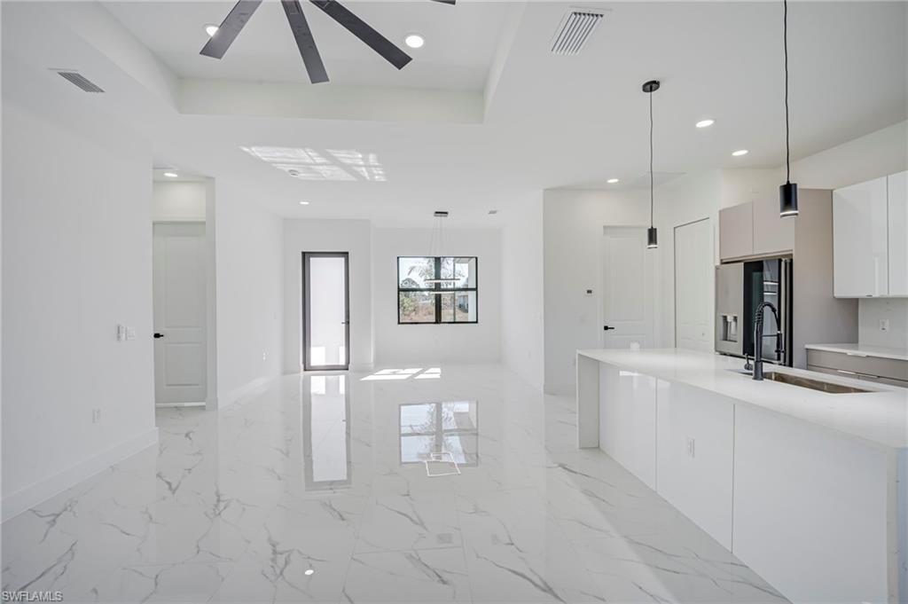 Kitchen featuring light marble finish floors, stainless steel fridge, white cabinets, pendant lighting, and light stone countertops