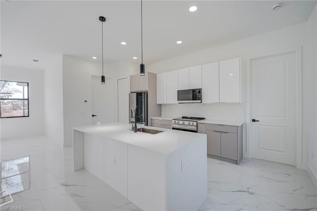 Dual tone kitchen featuring hanging light fixtures, stainless steel appliances, a center island with sink, light stone countertops, and two tone cabinets