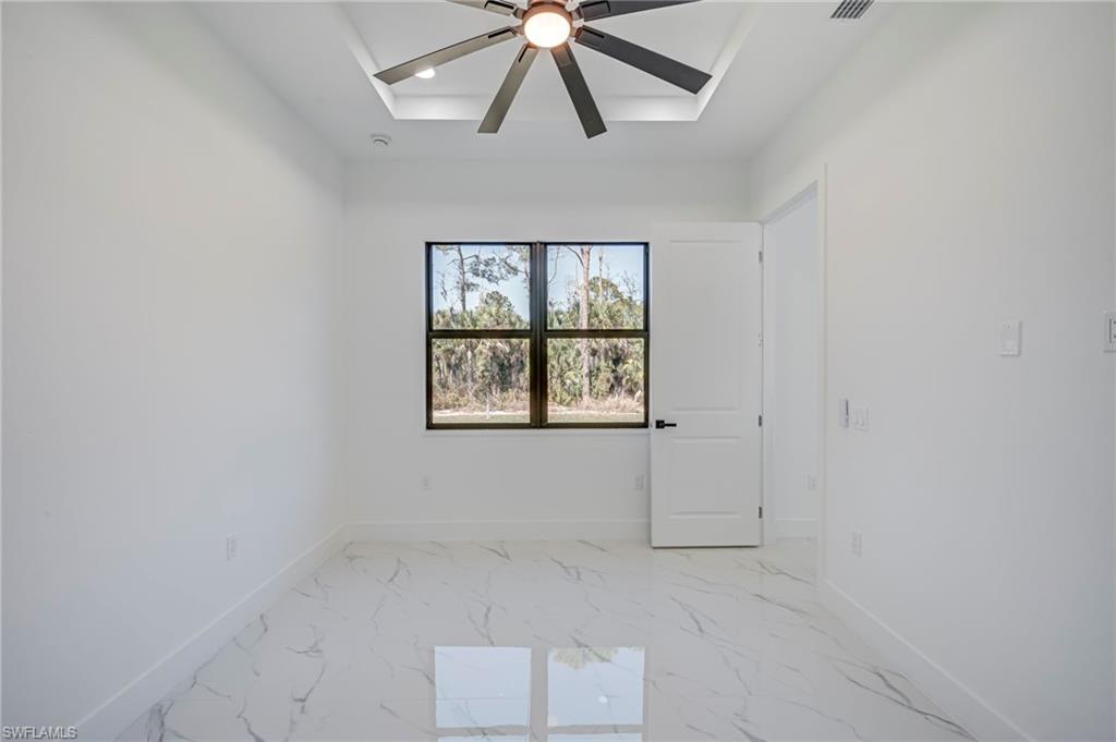 Empty room with ceiling fan, light marble finish flooring, and a raised ceiling