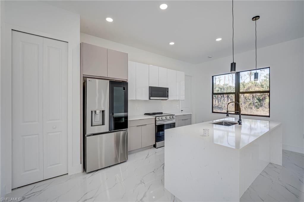 Kitchen with stainless steel appliances, decorative light fixtures, light marble finish floors, and light stone counters