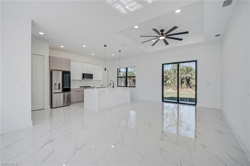 Kitchen with open floor plan, stainless steel appliances, an island with sink, light marble finish floors, and a ceiling fan