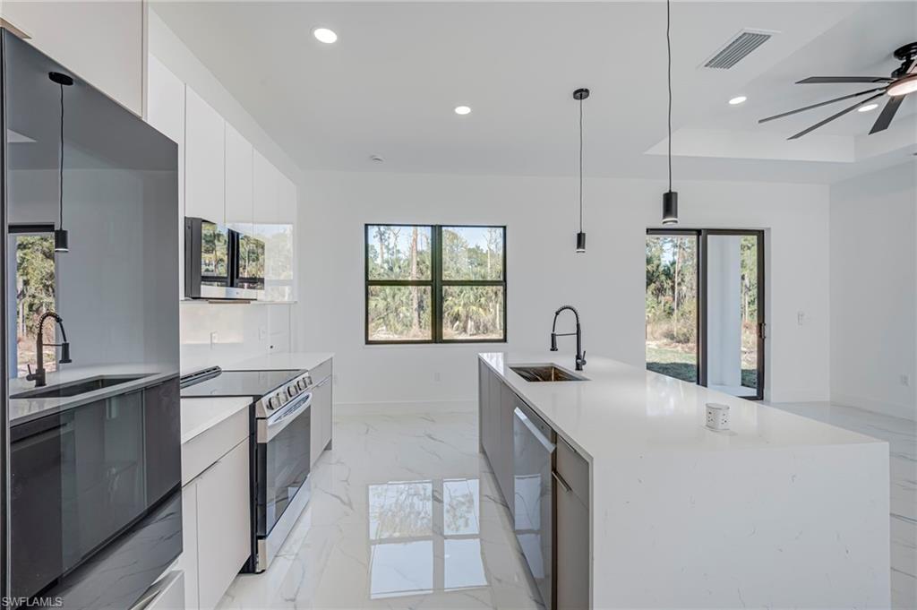 Dual tone kitchen featuring stainless steel appliances, light stone countertops, modern cabinets, a kitchen island with sink, and hanging light fixtures