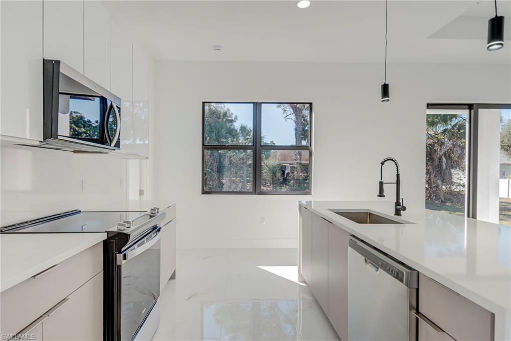 Kitchen with modern cabinets, stainless steel appliances, decorative light fixtures, and light stone countertops