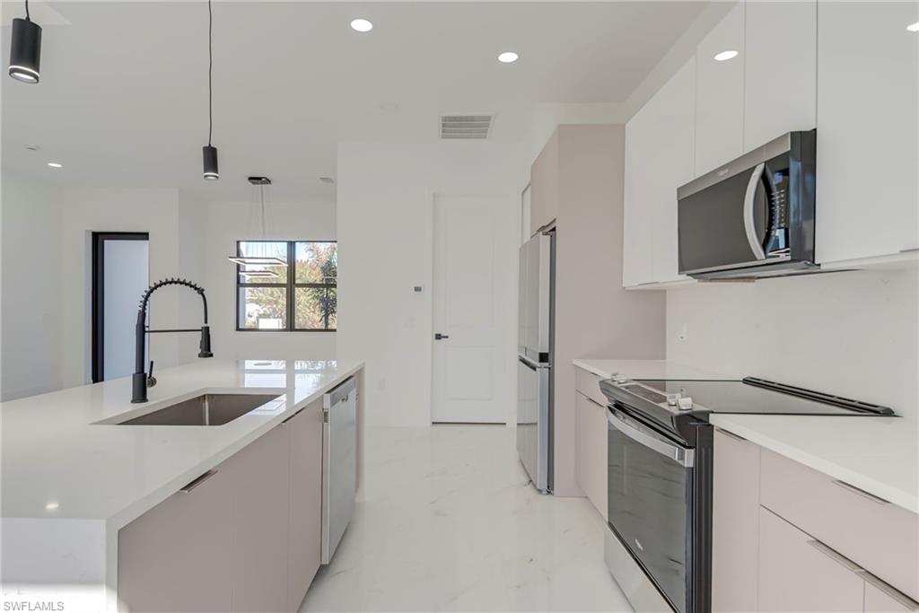 Kitchen with stainless steel appliances, pendant lighting, modern cabinets, white cabinetry, and light stone countertops