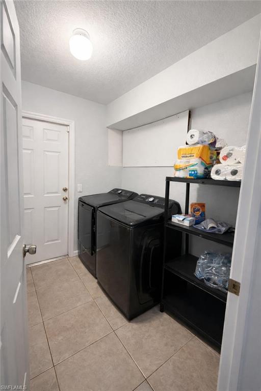 Laundry room with a textured ceiling, light tile patterned flooring, and independent washer and dryer