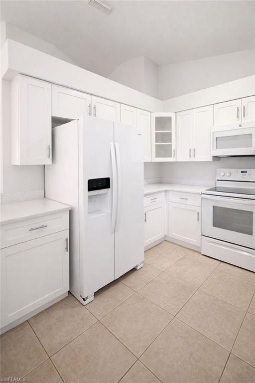 Kitchen with white appliances, white cabinets, glass fronted cabinets, and light tile patterned floors