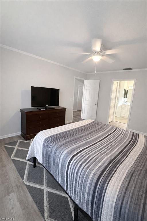 Bedroom with crown molding, ensuite bath, a ceiling fan, and wood finished floors