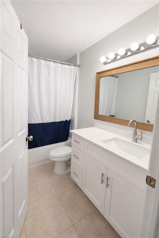 Bathroom with vanity, a textured ceiling, light tile patterned flooring, and shower / tub combo with curtain